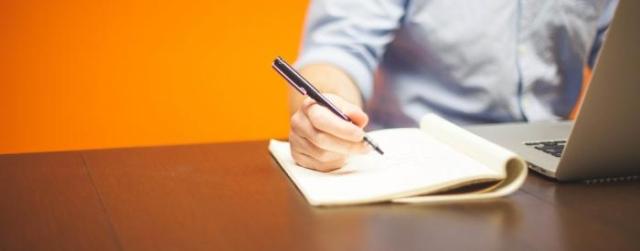 Man taking notes while looking at a laptop